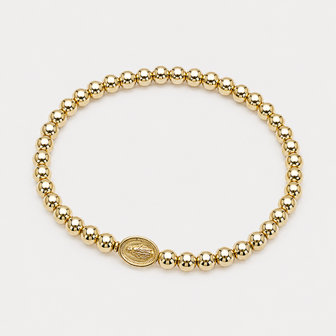 A gold beaded stretch bracelet with a small oval religious charm featuring a praying hands design, displayed on a clean white background.