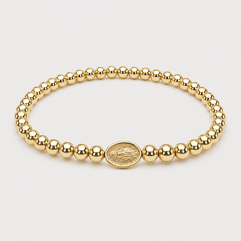 A gold beaded bracelet with a central oval religious medallion, displayed on a clean light gray background.