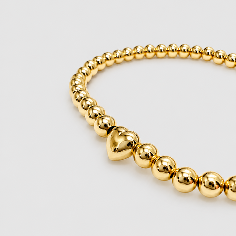 14K yellow gold ball bead stretch bracelet with solid puffed heart center station bead, high polish finish, close-up angled view