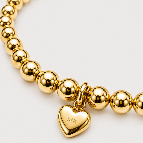 14K yellow gold puffed heart charm dangle on gold bead stretch bracelet, 14K hallmark stamp visible, close-up back view