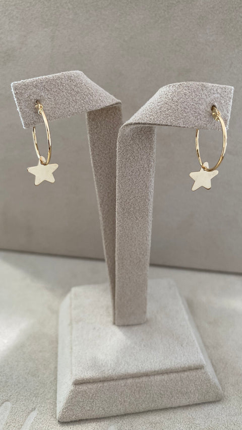 Pair of 14Kt yellow gold hoop earrings with dangling polished star charms, French lock closure on their stand