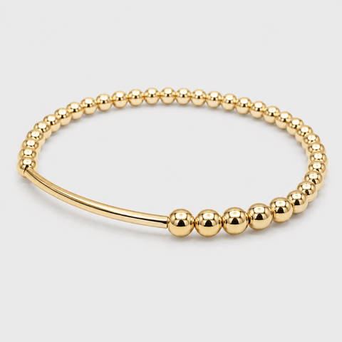 A polished gold bangle bracelet featuring a beaded outer band and a smooth inner band, photographed on a light gray background.