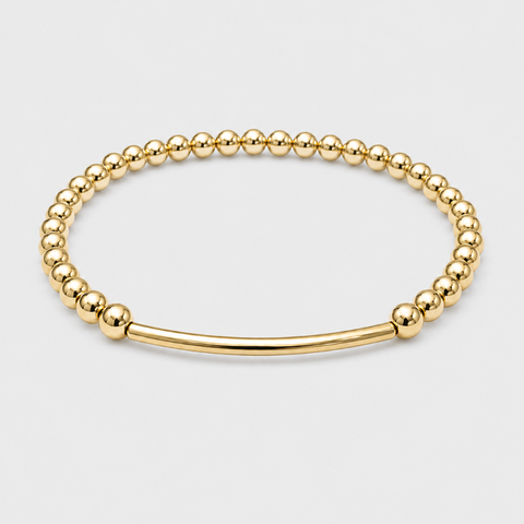 A polished gold-tone beaded stretch bracelet with a smooth bar clasp, displayed on a light gray background.