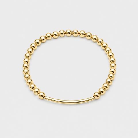 A gold beaded stretch bracelet with a smooth curved bar clasp, displayed on a light gray background.