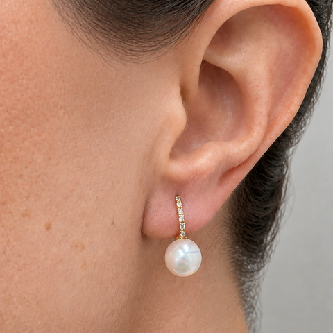 Model wearing 14K yellow gold pavé diamond huggie earring with white pearl drop close up ear lifestyle shot