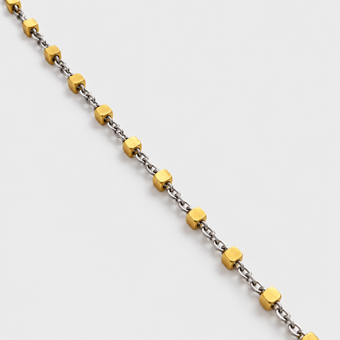 Close-up of polished yellow gold cube stations on a fine white gold chain necklace.