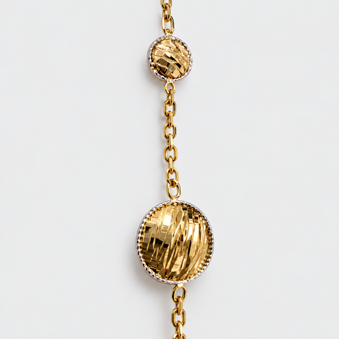 Close-up of textured diamond-cut gold discs and chain links on an 18K yellow gold station necklace.