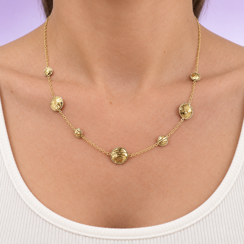 18K yellow gold diamond-cut disc station necklace worn at the neckline with a white top.
