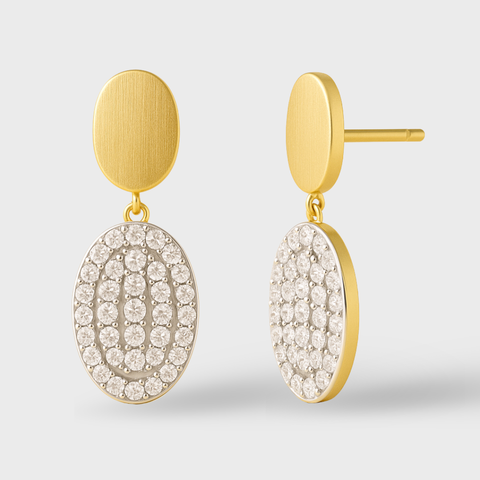 Gold earrings with circular, diamond-studded drops on a light gray background