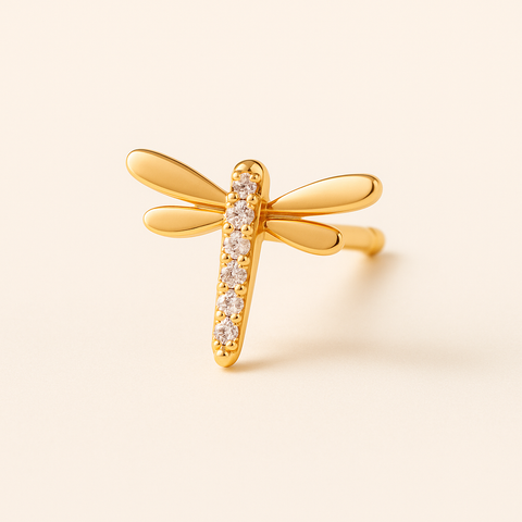 Dragonfly stud piercing laid flat on warm beige background and subtle shade