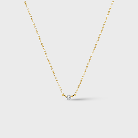 Gold necklace with a small diamond pendant on a light gray background