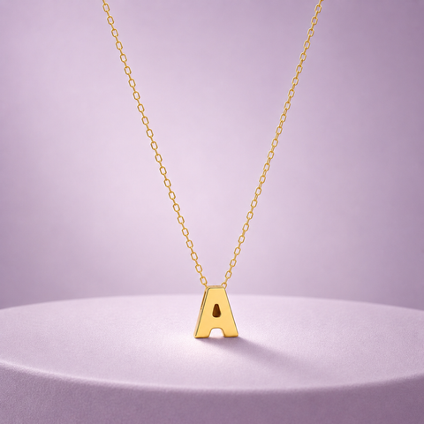 A gold initial necklace featuring a polished capital letter 'A' pendant on a delicate gold chain, displayed on a round lavender pedestal against a soft lavender background.
