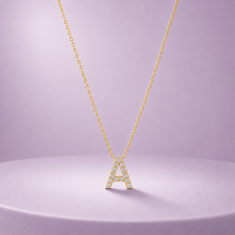 A gold initial necklace featuring the letter 'A' adorned with diamonds, displayed on a lavender-colored pedestal against a matching soft purple background.