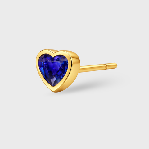 Gold heart-shaped earring with a blue gemstone on a light gray background
