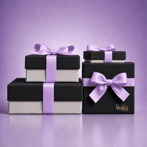 Three stacked gift boxes in black and white with light purple ribbons and bows, with the brand name 'Vaskia' printed in gold on the front box, set against a solid purple background.