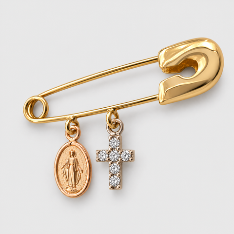 Angled view of a solid 18K yellow gold safety pin featuring a rose gold Miraculous Medal charm and a white gold diamond cross charm with a polished finish.