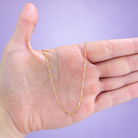Two-tone gold chain necklace with yellow gold cable links and textured white gold tube bead stations draped over an open palm on a lavender background, in-hand view showing spacing and chain scale