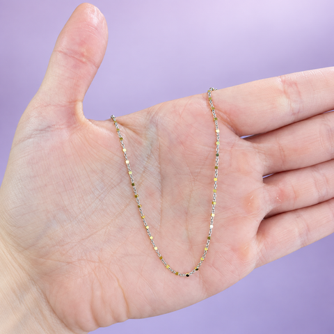 Two-tone gold chain necklace with white gold cable links and polished yellow gold cube bead stations draped over an open palm on a lavender background, in-hand view showing spacing and chain scale