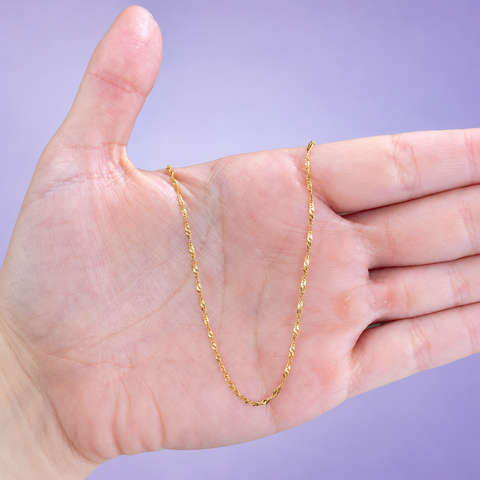 Yellow gold Singapore twist chain necklace with shimmering twisted links draped over an open palm on a lavender background, in-hand view showing sparkle and delicate chain scale
